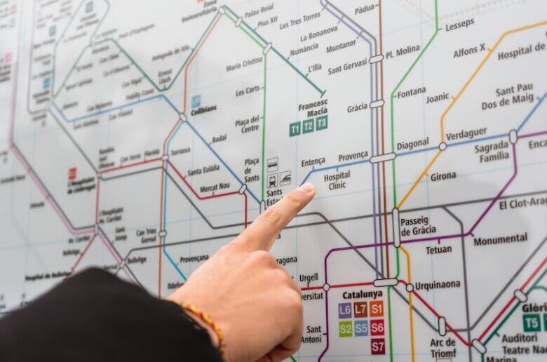 Unrecognizable person near information board pointing at map with colorful metro lines while choosing route for rise on street in city
